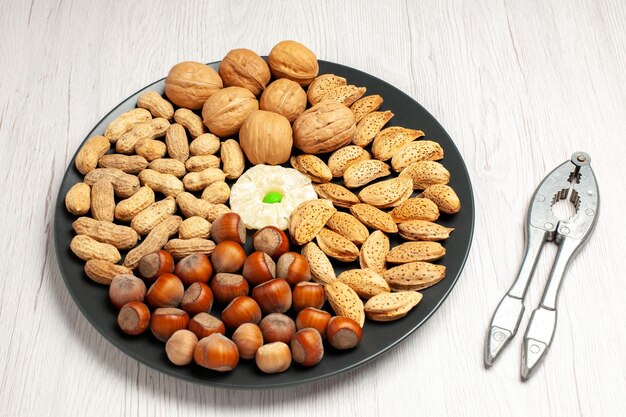 Vista superior de la composición de nueces nueces frescas cacahuetes y avellanas dentro de la placa en el escritorio blanco árbol de nueces planta de bocadillos muchos shell