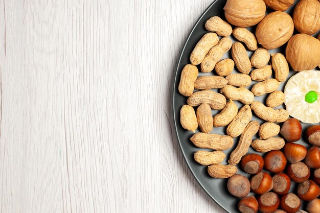 Vista superior de la composición de nueces nueces frescas cacahuetes y avellanas dentro de la placa en el escritorio blanco nueces planta de aperitivos árbol muchas conchas