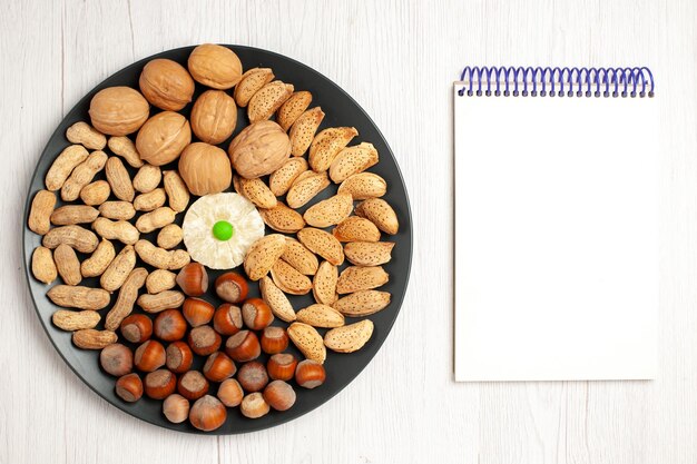 Vista superior de la composición de nueces nueces frescas cacahuetes y avellanas dentro de la placa en el escritorio blanco planta de aperitivos tuerca árbol muchos shell