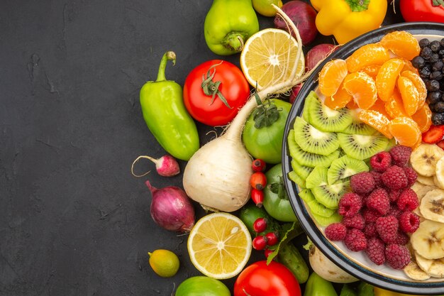 Vista superior de la composición vegetal verduras frescas con frutas en rodajas sobre un fondo oscuro, planta de vida, dieta madura, color de ensalada de alimentos