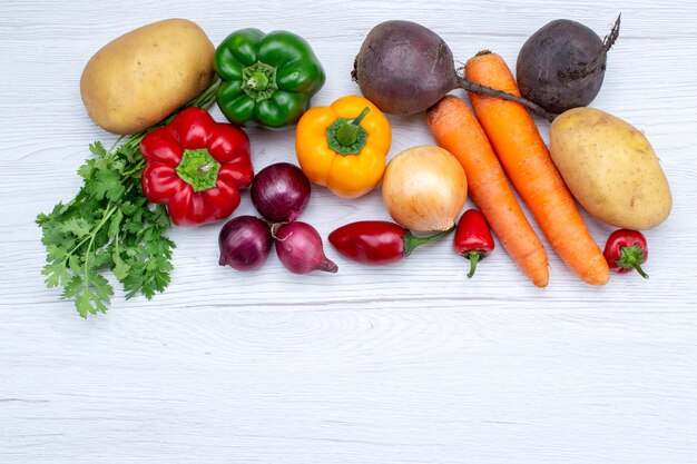 Vista superior de la composición vegetal con verduras frescas, zanahorias, cebollas y patatas en el escritorio blanco comida comida ensalada de verduras frescas