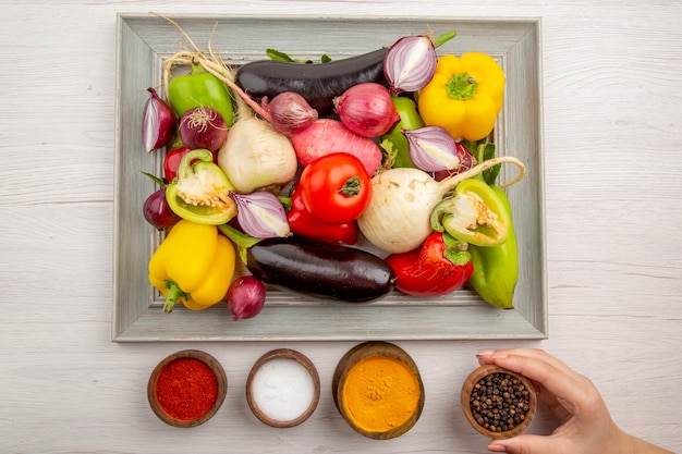 Vista superior de la composición de verduras frescas con condimentos en la mesa blanca