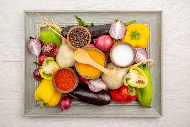 Vista superior de la composición de verduras frescas con condimentos en la mesa blanca