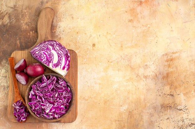 Vista superior del concepto de comida sana con un poco de repollo picado y cebollas rojas en una tabla de cortar para la preparación de ensalada de verduras en una mesa de madera con espacio de copia