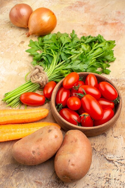 Vista superior concepto de ingredientes de cocina con tomates roma, patatas, cebollas, zanahoria y un manojo de perejil para ensalada sobre un fondo de madera