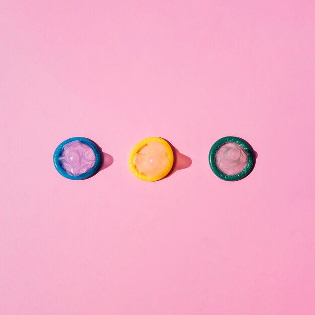 Vista superior de condones de colores sobre fondo rosa