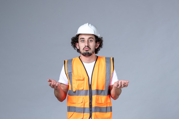 Vista superior del constructor masculino curioso con chaleco de advertencia con casco de seguridad en la pared de onda gris