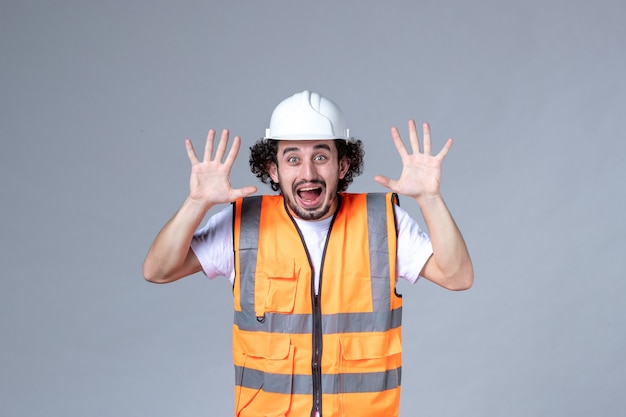 Foto gratuita vista superior del constructor masculino happu con chaleco de advertencia con casco de seguridad en la pared gris de la onda