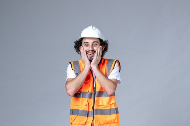Vista superior del constructor masculino sonriente con chaleco de advertencia con casco de seguridad en la pared de onda gris