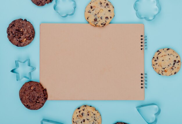 Vista superior de las cookies alrededor del bloc de notas sobre fondo azul con espacio de copia