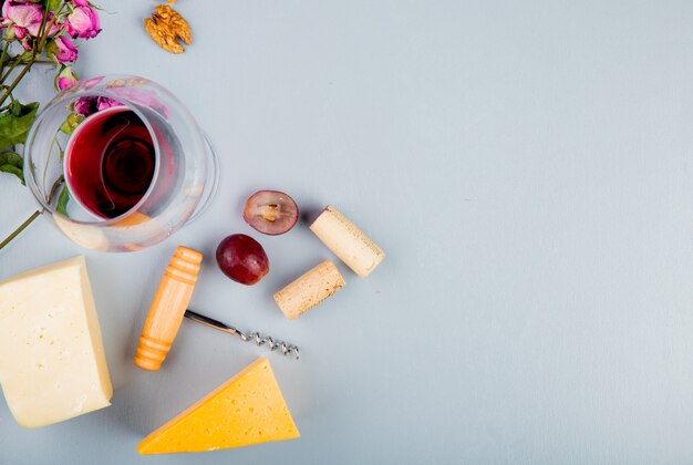 Vista superior de una copa de vino tinto con queso corchos de uva sacacorchos de nuez y flores en blanco con espacio de copia