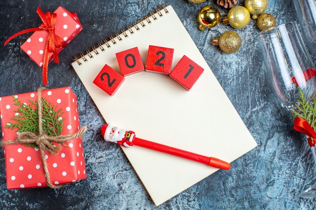 Vista superior de las copas de cristal caídas con cinta roja y accesorios de decoración junto al cuaderno de cajas de regalo con números sobre fondo oscuro