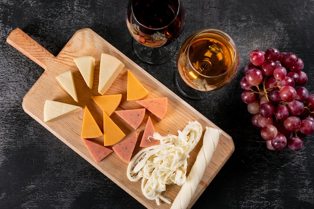 Vista superior de copas de vino y queso en tabla de cortar de madera en horizontal oscuro