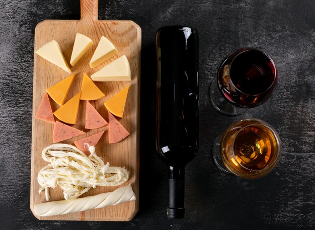 Vista superior de copas de vino y queso en tabla de cortar de madera en horizontal oscuro