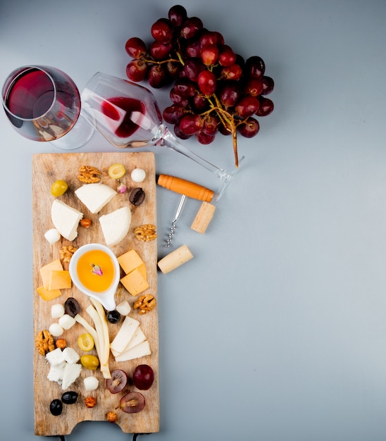 Foto gratuita vista superior de copas de vino tinto con queso uva mantequilla de nueces en tabla de cortar y sacacorchos en blanco con espacio de copia