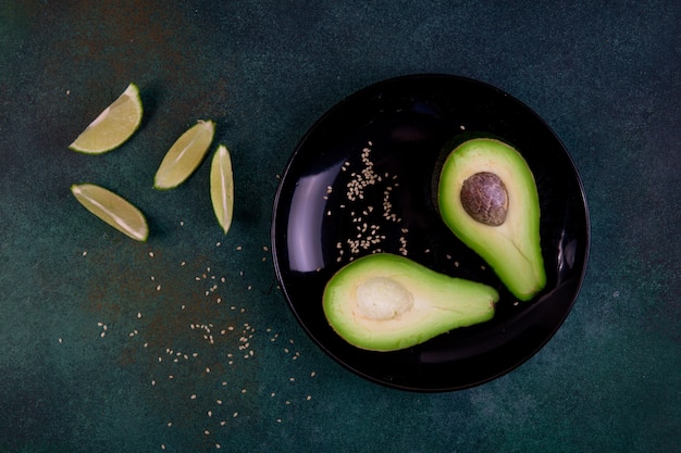 Vista superior copia espacio cortado en medio aguacate en un plato con semillas de sésamo y limón sobre un fondo verde oscuro