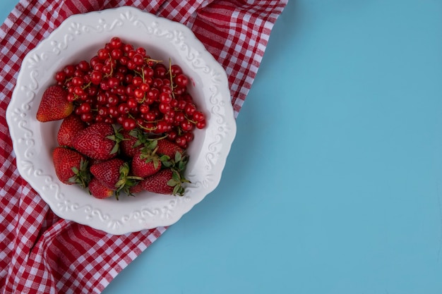 Vista superior copia espacio fresas con grosella roja en un plato con una toalla de cocina roja sobre un fondo azul claro