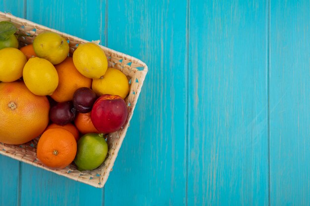 Vista superior copia espacio mezcla de frutas pomelo limones limas naranjas melocotones y ciruelas en una canasta sobre un fondo turquesa