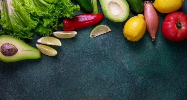 Vista superior copia espacio mezcla de verduras aguacate limón pimiento rojo cebolla y lechuga sobre un fondo verde oscuro