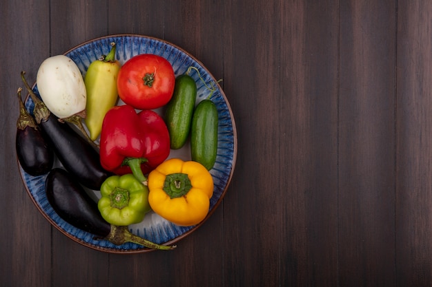 Foto gratuita vista superior copia espacio pimientos de colores con pepinos y tomates berenjenas en un plato sobre fondo de madera