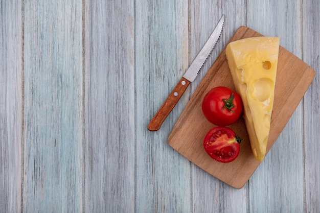Vista superior copia espacio queso maasdam con tomates en un soporte con un cuchillo sobre un fondo gris