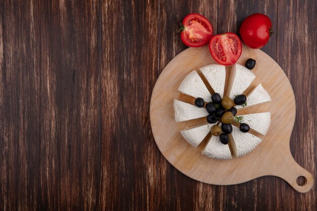 Vista superior copia espacio rebanadas de queso feta con aceitunas en un soporte y tomates sobre fondo de madera