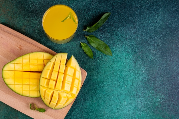 Vista superior copia espacio en rodajas de mango en la pizarra con un vaso de jugo de naranja y hojas de menta