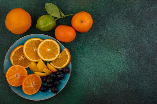 Vista superior copia espacio rodajas de naranja con cerezas dulces en una placa azul con mandarinas sobre un fondo verde
