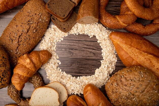 Vista superior de copos de avena en forma circular y panes alrededor como bagel de mazorca de centeno blanco baguette sobre fondo de madera con espacio de copia