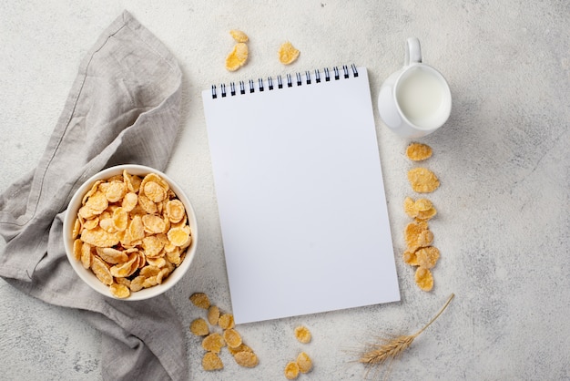 Foto gratuita vista superior de copos de maíz de desayuno con cuaderno y leche