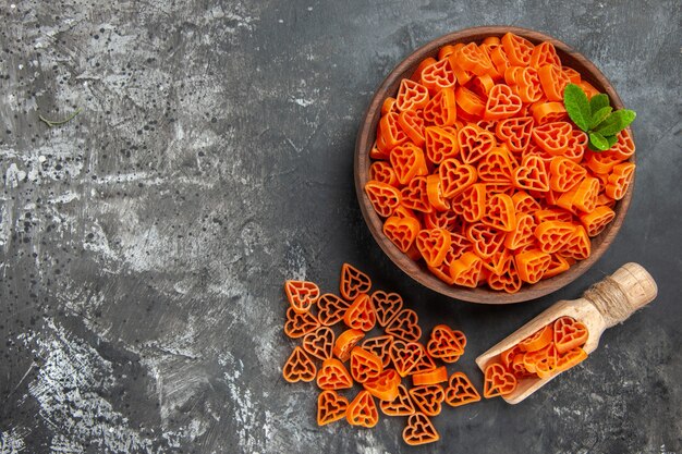 Vista superior de corazones rojos de pasta italiana en un cuenco, cuchara de madera en el lugar de copia de mesa oscura