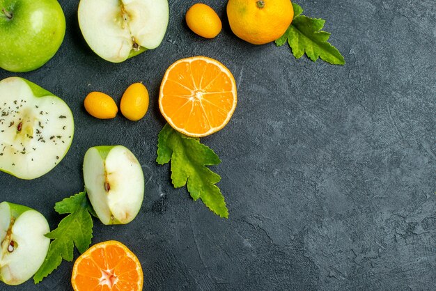 Vista superior cortadas manzanas y mandarinas hojas cumcuat en el espacio libre de la mesa oscura