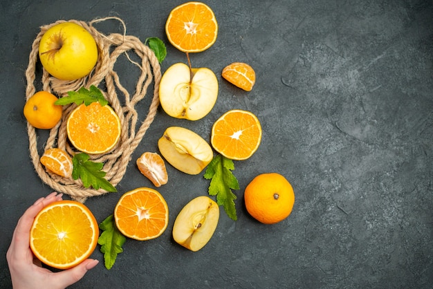 Vista superior cortadas naranjas y manzanas cortadas naranja en mano femenina sobre superficie oscura