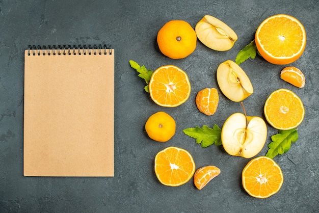 Vista superior cortar naranjas y manzanas un cuaderno sobre fondo oscuro