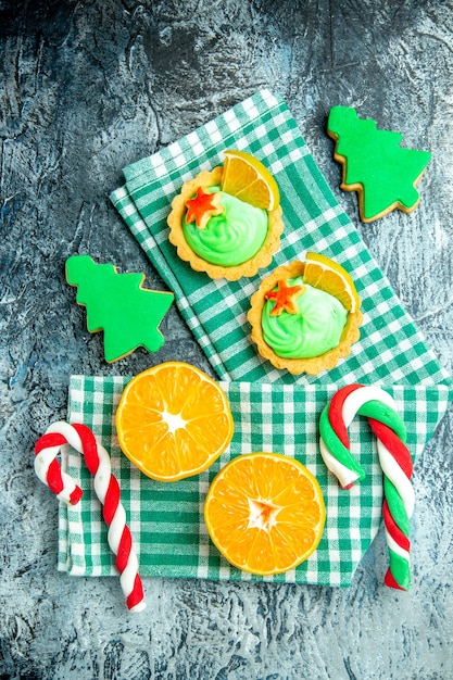 Vista superior cortó naranjas dulces de árbol de Navidad tartas pequeñas en una toalla de cocina a cuadros blanca verde sobre una mesa gris