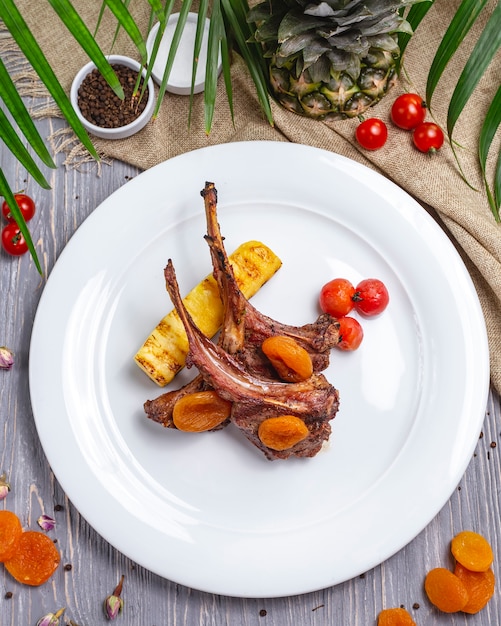 Vista superior costillas de cordero a la parrilla con berenjenas tomates cherry albaricoques secos en un plato