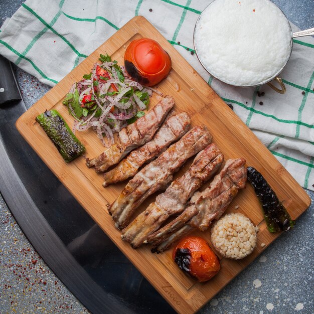 Vista superior costillas de kebab con verduras fritas y cebolla picada y ayran y cuchillo en tabla de cortar