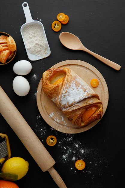 Vista superior de croissant en salvamanteles con cuchara de mandarina de limón kumquat de harina de huevo y rodillo sobre fondo negro