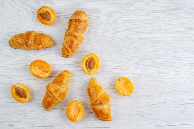 Una vista superior de croissants de albaricoque con albaricoques frescos en el escritorio blanco pastel de frutas