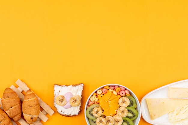 Vista superior de croissants con frutas queso, tostadas y copia espacio sobre fondo amarillo horizontal