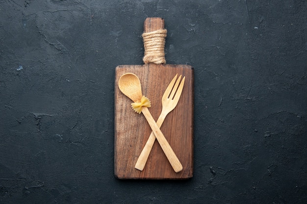 Vista superior cruzó la cuchara de madera y el tenedor en el tablero de madera para servir en el lugar de copia de la mesa oscura