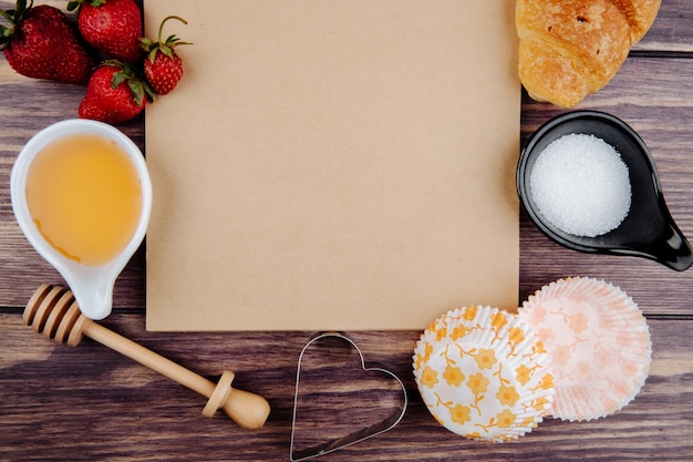 Vista superior del cuaderno de bocetos y fresas frescas maduras con croissant de azúcar de miel y cortadores de galletas en madera