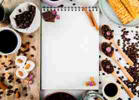 Foto gratuita vista superior de un cuaderno de bocetos y granos de café en un tazón de madera y cucharas y con trozos de chocolate lokum y granos de café esparcidos sobre fondo rústico