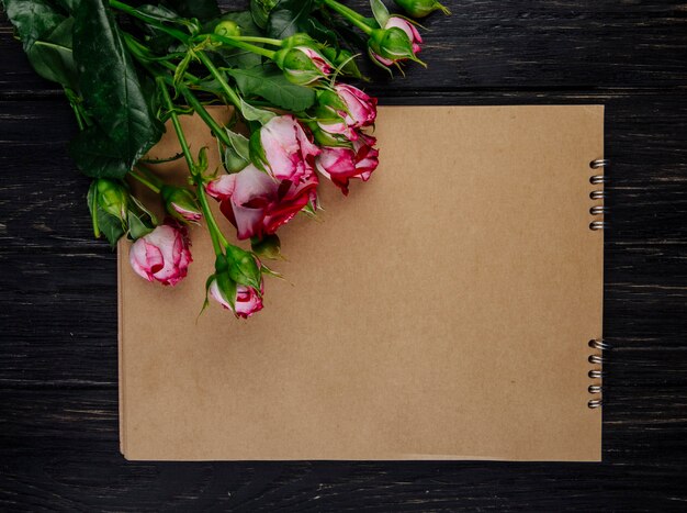 Vista superior de un cuaderno de bocetos con rosas de color rosa con brotes sobre fondo de madera oscura