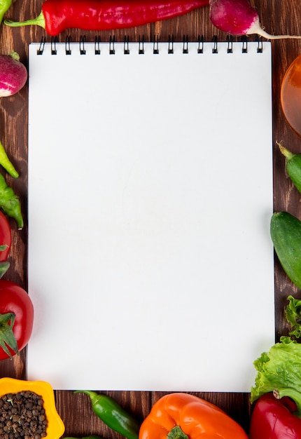 Vista superior del cuaderno de bocetos y verduras frescas pimientos coloridos chiles verdes tomates y granos de pimienta negra en madera rústica