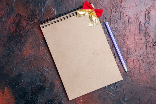 Vista superior de un cuaderno con bolígrafo de lazo pequeño en una mesa de color rojo oscuro con lugar para copiar