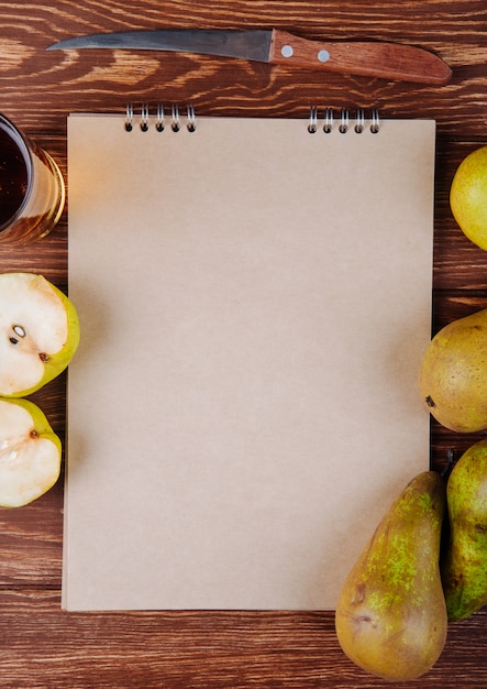 Vista superior de un cuaderno de dibujo y peras maduras frescas con un vaso de jugo de pera sobre fondo de madera