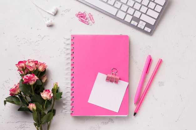 Vista superior del cuaderno en el escritorio con ramo de rosas y bolígrafos