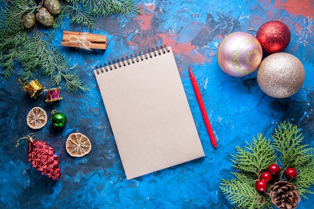 Vista superior cuaderno lápiz ramas de abeto conos juguetes de árbol de Navidad en superficie azul