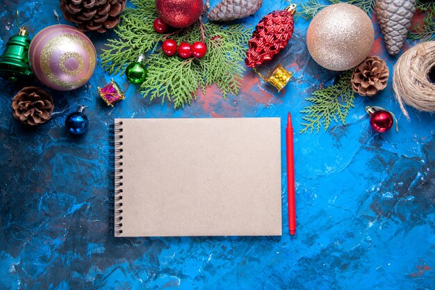 Vista superior cuaderno lápiz rojo ramas de abeto conos juguetes de árbol de Navidad en superficie azul